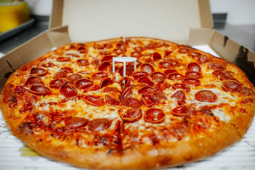 A whole pepperoni pizza with melted cheese in an open cardboard delivery box.